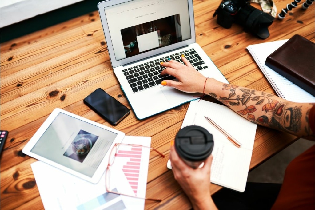 Personne qui travaille sur un ordinateur et des fichiers papier, café à la main.