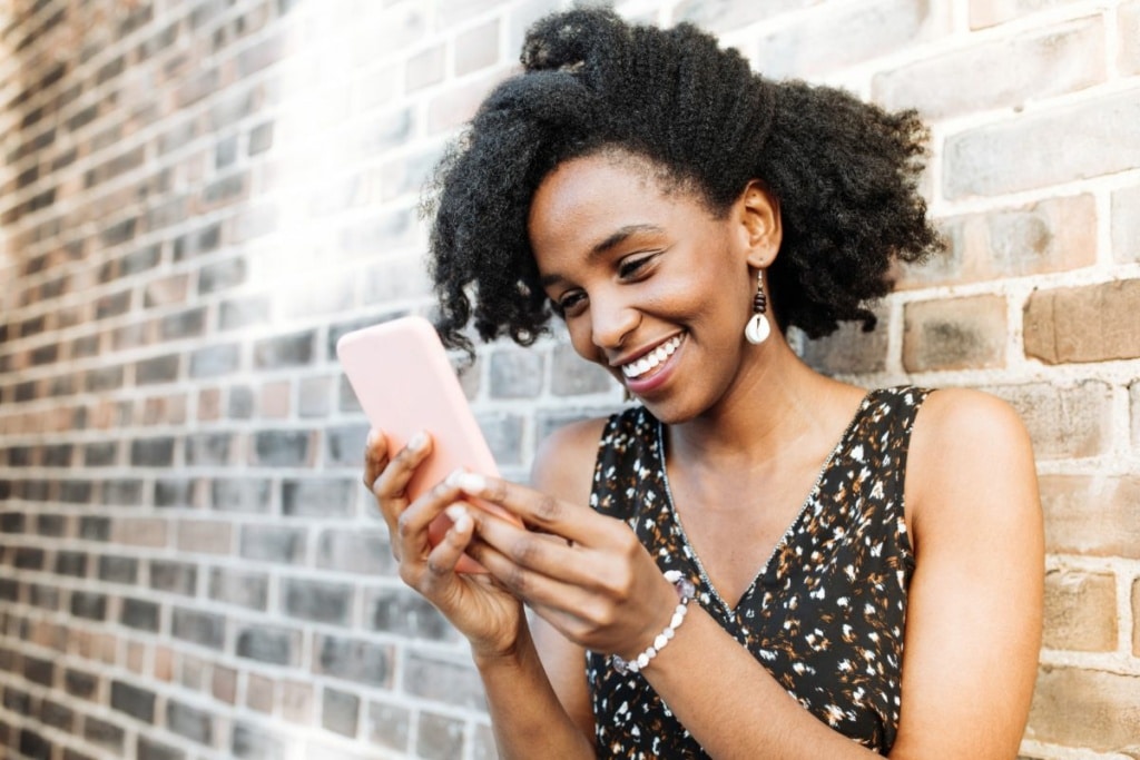 Une femme sourit en envoyant des messages depuis son téléphone