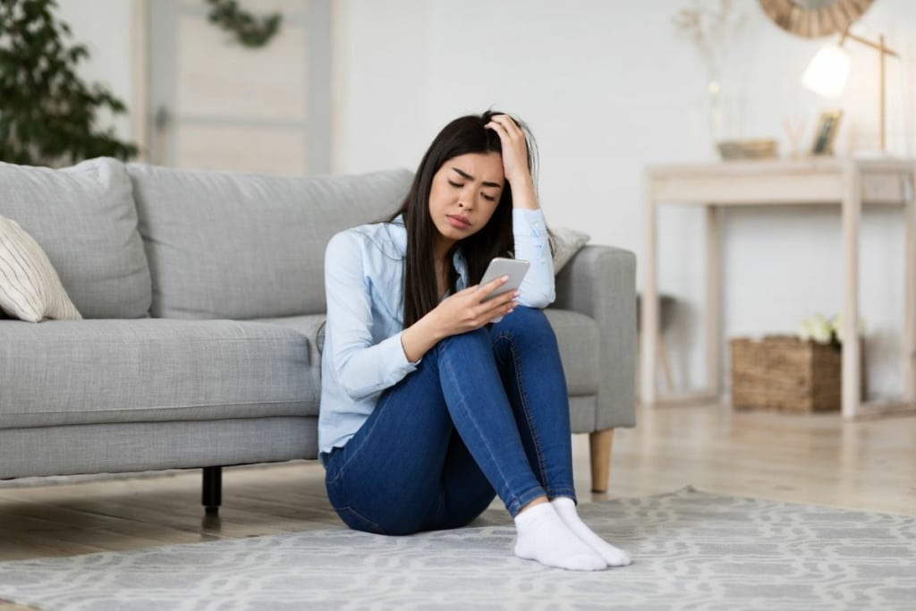 Femme soucieuse assise au sol, regarde son téléphone