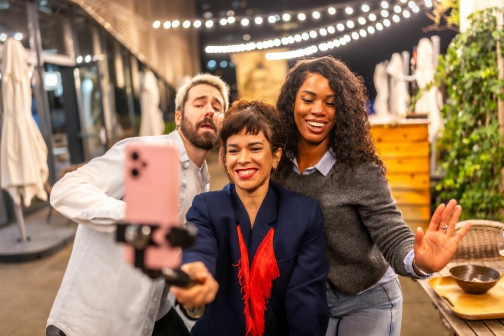 Trois personnes posent devant un téléphone avec une perche à selfie