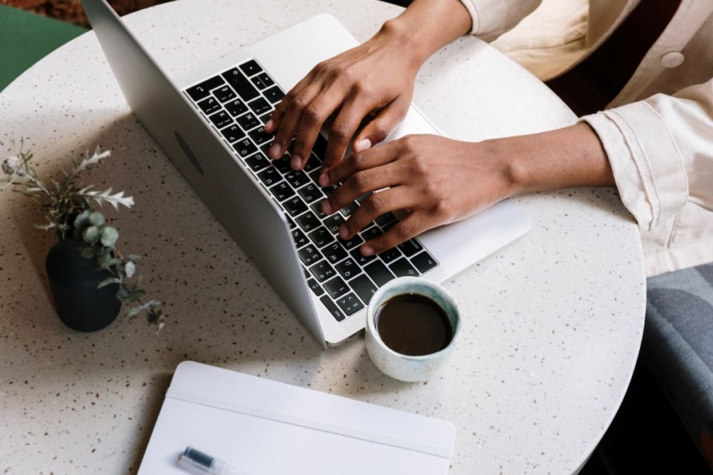 Mains sur ordinateur posé sur une table près d'une tasse de café