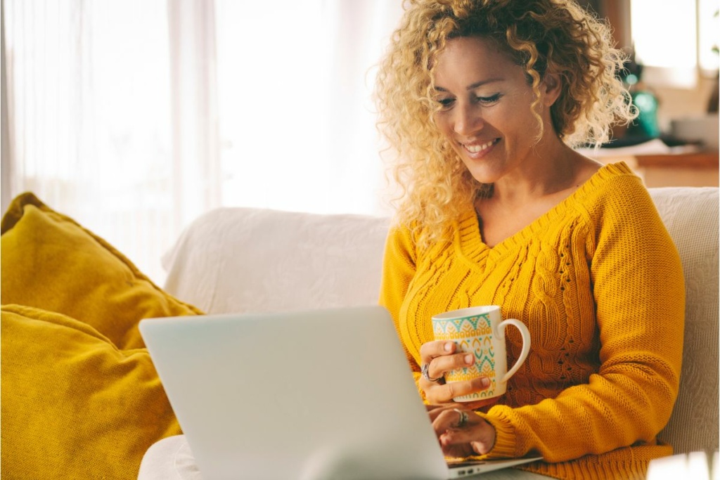 Une femme boit un café devant son ordinateur.